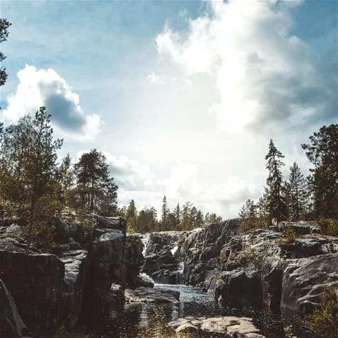 En ström med kristallklart vatten flyter fram mellan stora klippor och stenblock i en naturskön omgivning vid Storforsens camping, omgiven av vildmark och berg.