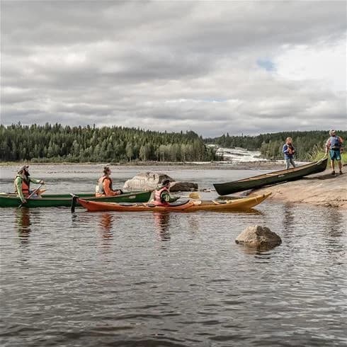 En person paddlar en kajak på en stilla sjö omgiven av grönskande skog vid Storforsens camping.