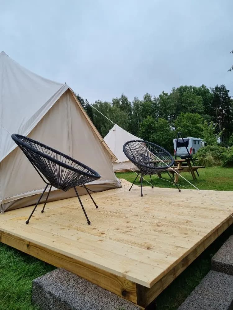 En campingplats med tält och utomhusmöbler på en trädäckad yta omgiven av träplank.