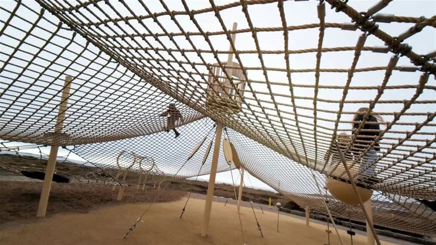 En nätgunga vid en sandig strand med rep och sanddyner i bakgrunden, Apelvikstrand.