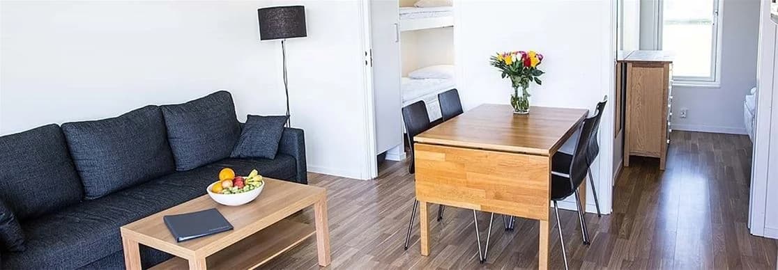 En inbjudande inomhusmiljö vid Apelvikstrand, som visar ett rum med trägolv och trädetaljer i inredningen. Trämöbler och naturnära färger skapar en varm och hemtrevlig atmosfär i en lägenhet vid kusten.