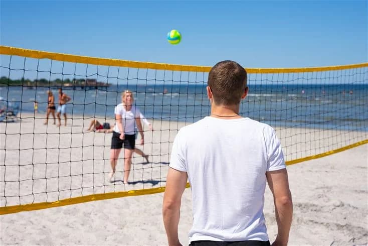 En grupp människor spelar beachvolleyboll på Grönhag Camping, med ett volleybollnät i förgrunden och spelare klädda i shorts.