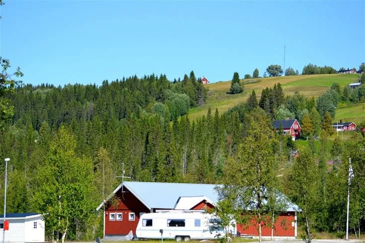 En lantlig campingplats vid Åkersjöstrand med stugor och tältplatser omgivna av skog och öppna landskap. Träd och grönska pryder området, vilket ger en avkopplande och naturnära atmosfär.