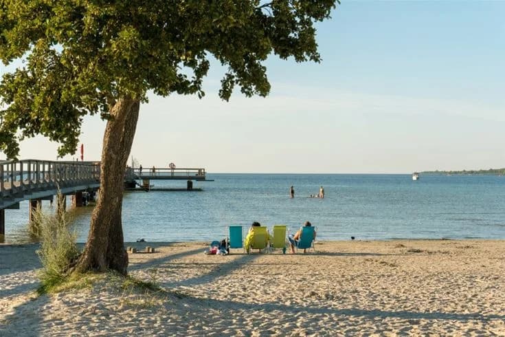 En strand med sand och en kustlinje som möter ett lugnt hav under en klar sommarhimmel.