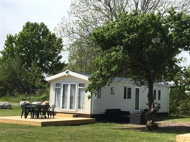 En campingplats med gröna gräsmattor och trädgårdsbyggnader, där mobila hem är uppställda bland de välskötta ytorna.