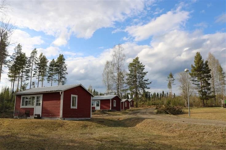 En mysig stuga i trä ligger inbäddad i en lummig, grönskande landsbygdsmiljö med gräs och träd. Campingområdet omges av vidsträckta fält och erbjuder en fridfull atmosfär.