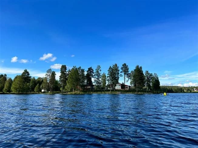 En lugn sjö omgiven av grönskande natur under en klarblå sommarhimmel.