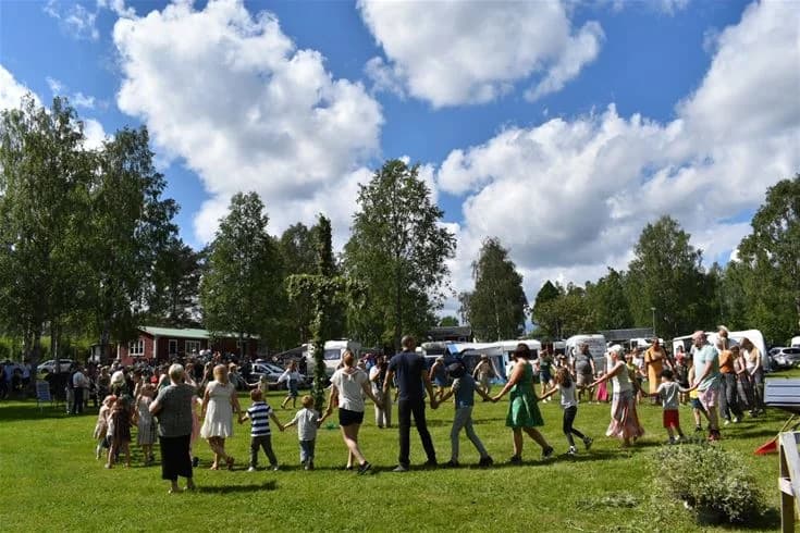 En solig dag på Trehörningsjö Camping & Stugor med människor samlade i en skogsdunge, deltog i olika fritidsaktiviteter.