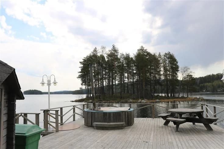 En naturskön utsikt över en sjö med en träbrygga som sträcker sig ut över vattnet, omgivet av frodig grönska och skog, vid Trehörningsjö Camping & Stugor.