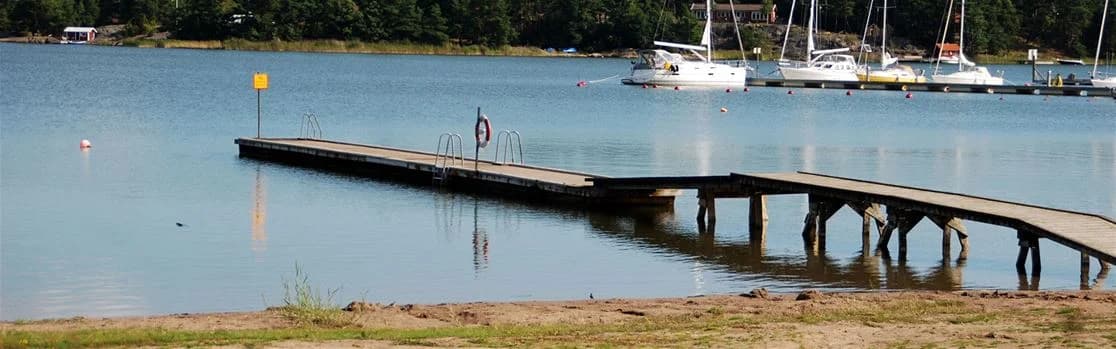 En bild från Arkösunds camping som visar en småbåtshamn vid en kropp av vatten. Flera båtar ligger förtöjda vid bryggorna, omgivna av sjö och grönska.
