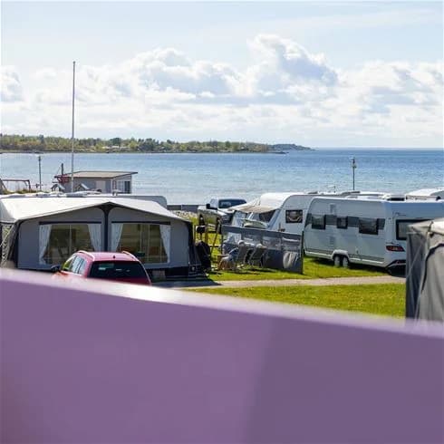 En kustnära campingplats med husvagnar och husbilar parkerade på en grusplan nära havet.