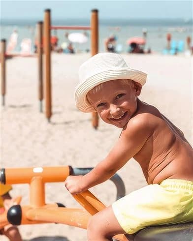 Ett glatt barn bär en solhatt och ler under en sommardag på Klinta Camping, vilket visar en känsla av semester och glädje.