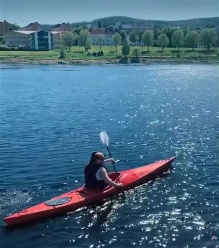 En person paddlar en kajak på en lugn sjö omgiven av grönskande skog, vilket erbjuder en fridfull naturupplevelse vid Sollefteå camping.