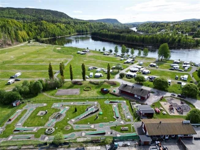 Fågelperspektiv av Sollefteå camping med grönskande parklandskap, stigar och vägar i korsning, samt omgivande landsbygd.