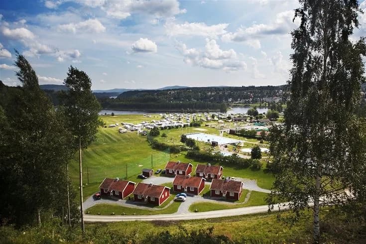 Luftfoto över Sollefteå Camping med gröna gräsmattor och omgivande landskap, parker och byar i närheten.