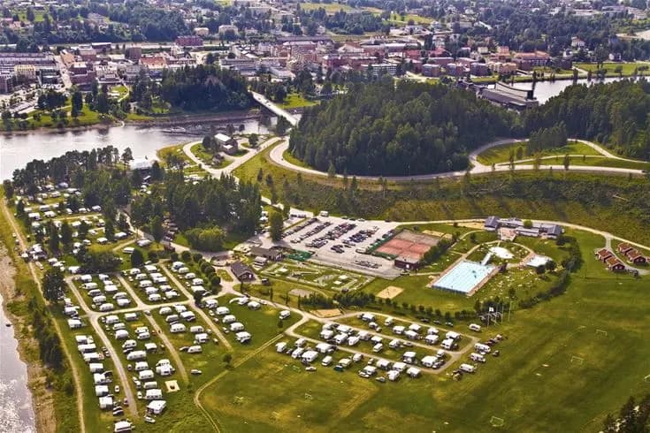 Flygbild över Sollefteå Camping och dess omgivningar. Området visar en blandning av gröna parker, bostadshus och det omgivande landskapet, vilket skapar en naturskön miljö för campingbesökare.