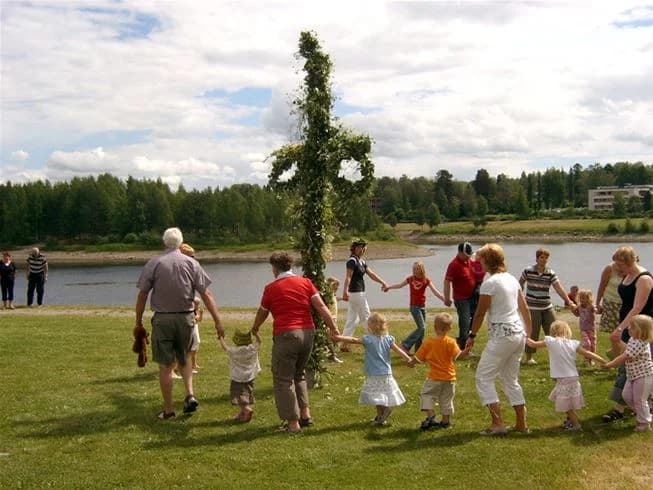 En grupp människor njuter av fritidsaktiviteter vid en sjö i Sollefteå camping, omgiven av gröna kullar och skog.