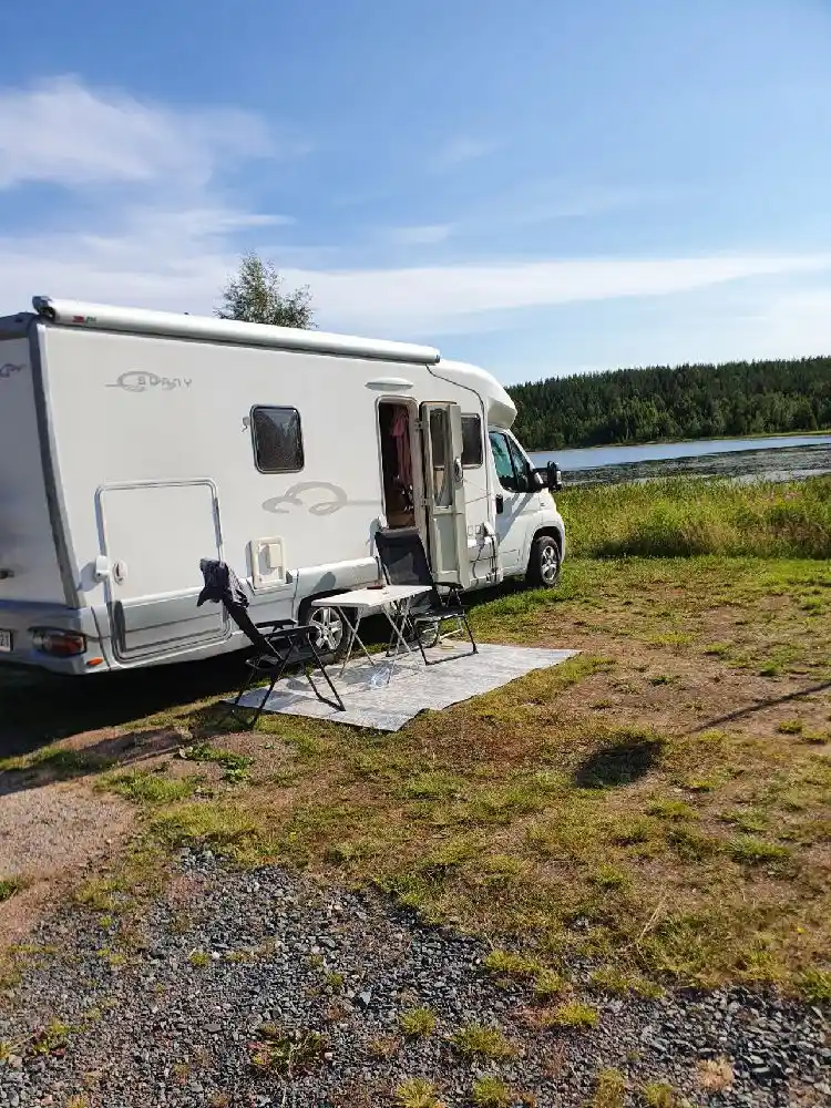 En campingplats med flera husbilar och husvagnar uppställda, omgiven av grönska och träd, typiskt för en idyllisk svensk campingupplevelse.
