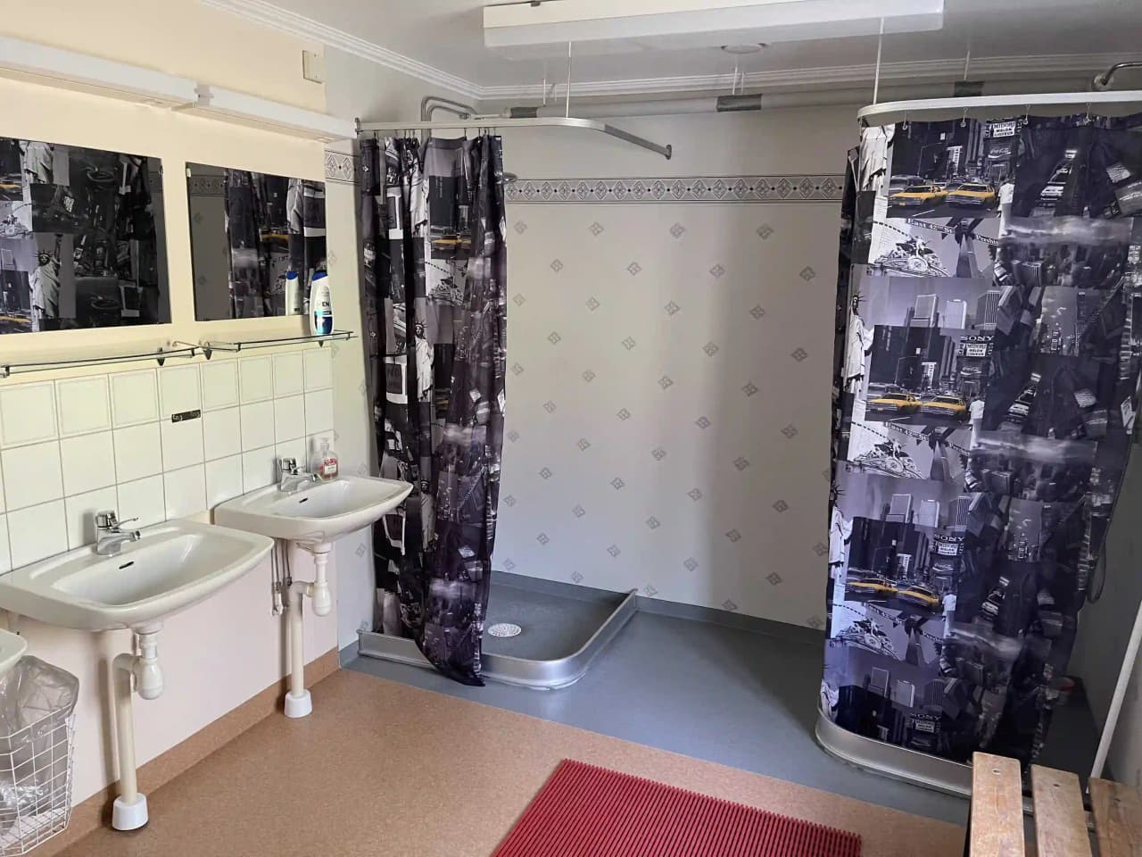 Bild av ett badrum på Gammeltomtens camping. Rummet har ett kaklat golv och tak med en TV, en vit handfat med ett kran. På sidan finns en dusch med ett duschdraperi.