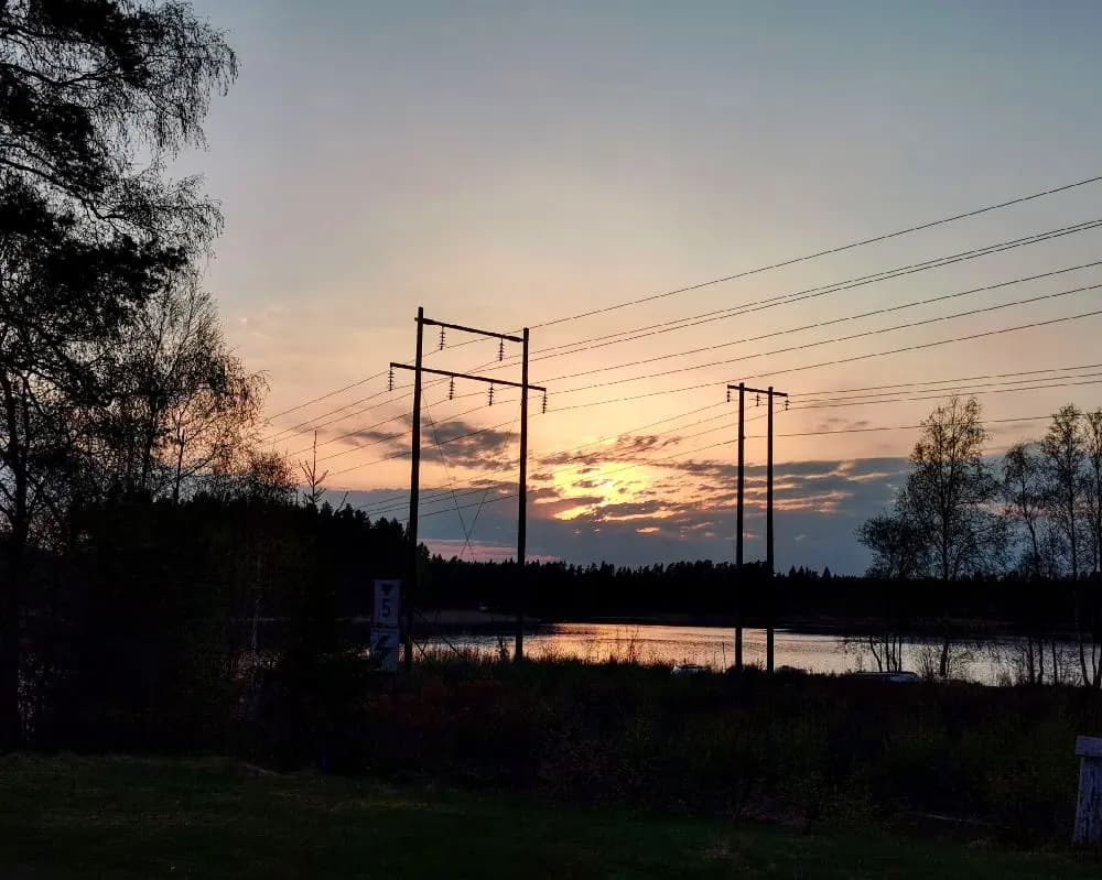 En vacker solnedgång vid Hjortsjöns camping med telefonnät som sträcker sig över landskapet. En himmel i skymning, fylld av mjuka moln, bildar en färgstark bakgrund som fångar naturens stillhet.