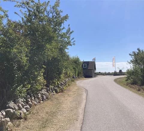 Bild av en asfalterad väg som leder in i Wikegårds Semesterby & Ställplatscamping, omgivet av klarblå himmel.