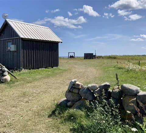En vidsträckt gräsmatta i en lantlig miljö med ett enkelt skjul i bakgrunden, omgiven av öppna fält och ängar vid Wikegårds semesterby & ställplatscamping.