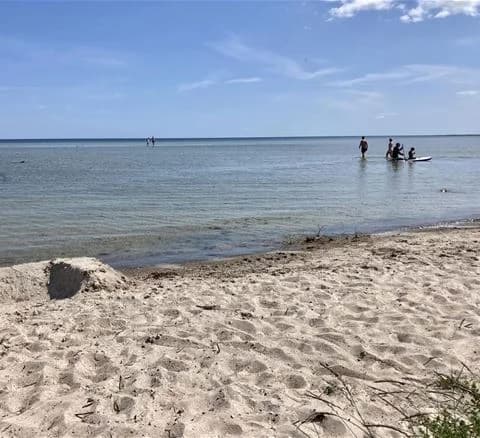 En somrig strand med sand och kustlinje vid Wikegårds semesterby & ställplatscamping. Havet sträcker sig mot horisonten, perfekt för en avkopplande semesterupplevelse.