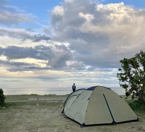 En vy över Wikegårds semesterby & ställplatscamping med tält uppsatta på en sandig campingplats vid kusten. I bakgrunden syns det omgivande landskapet och utrustning för friluftsliv.