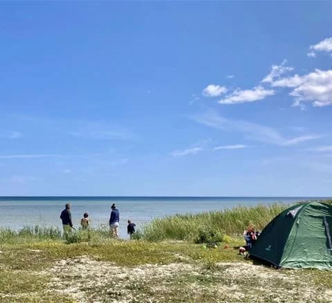 En solig sommardag vid kusten vid Wikegårds semesterby & ställplatscamping, med campingutrustning uppställd nära havet och en vacker utsikt över stranden och kusten.