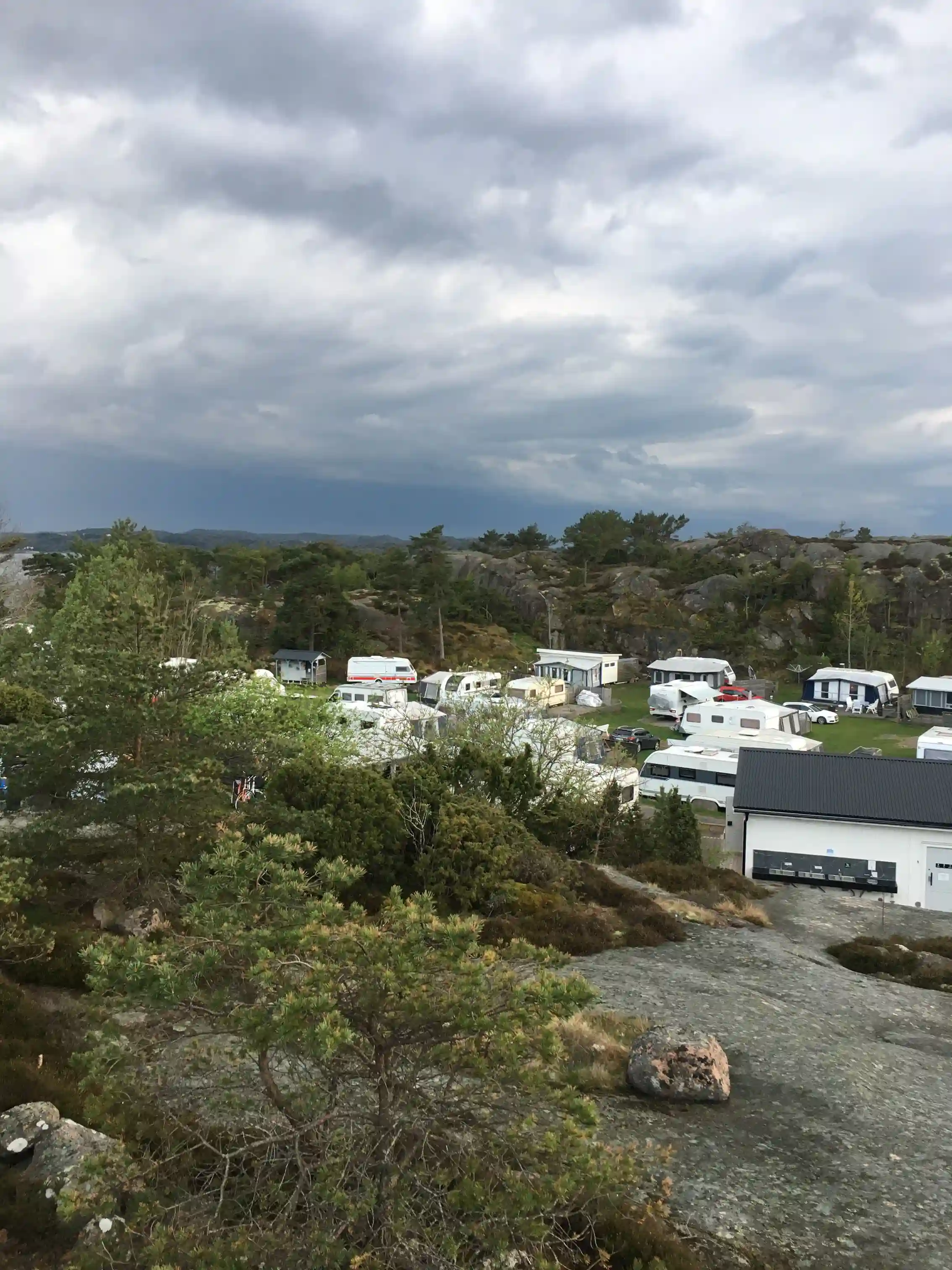 En husbil parkerad på en naturskön campingplats i Fjällbacka, omgiven av kuperad terräng och under en himmel med vita cumulusmoln.