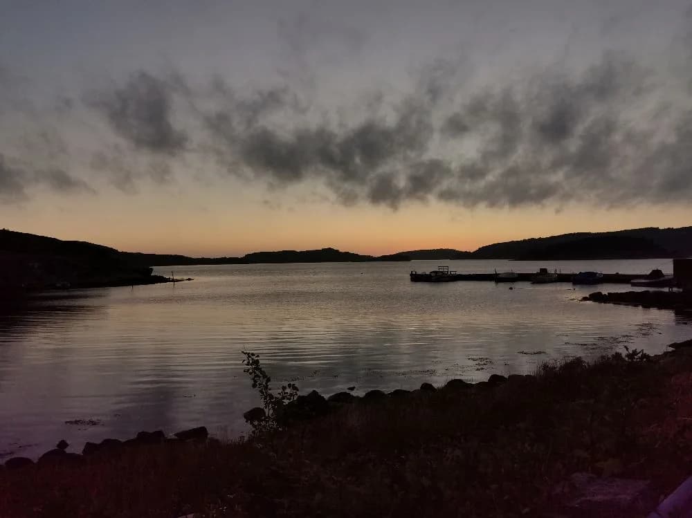 En naturskön bild över Fjällbacka camping vid skymning, med en himmel i dova färger och vatten som lugnt breder ut sig mot horisonten.
