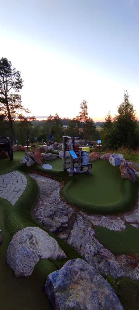 En lummig trädgård med en välskött gräsmatta och anlagda växter, typisk för en campingmiljö, med inslag av minigolf och rekreationsområden.