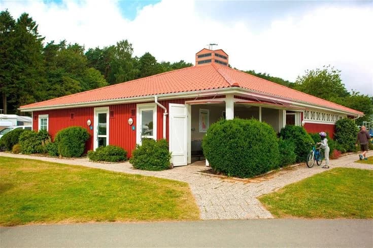 En mysig stuga på Lisebergs camping Askim strand, omgiven av frodig grönska med välskötta buskar och gräsmattor.