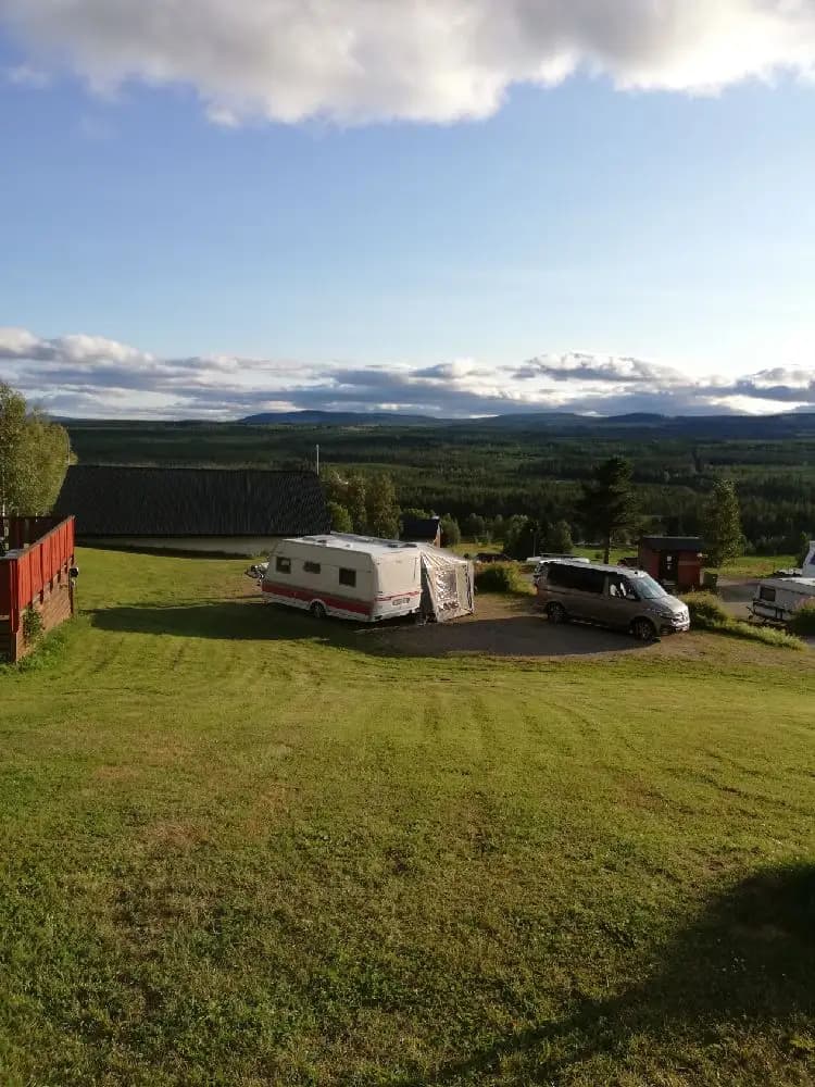 En campingplats vid Kvarnsjö Camp med ett tält och en husvagn uppställda på en grön gräsmatta, omgiven av vidsträckta fält och med en klar himmel som är prydd med cumulusmoln.