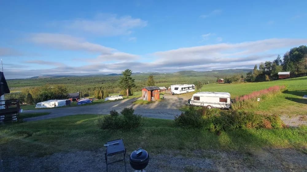 En vidsträckt äng vid Kvarnsjö Camp med grönskande gräsmarker under en himmel fylld med vita cumulusmoln.