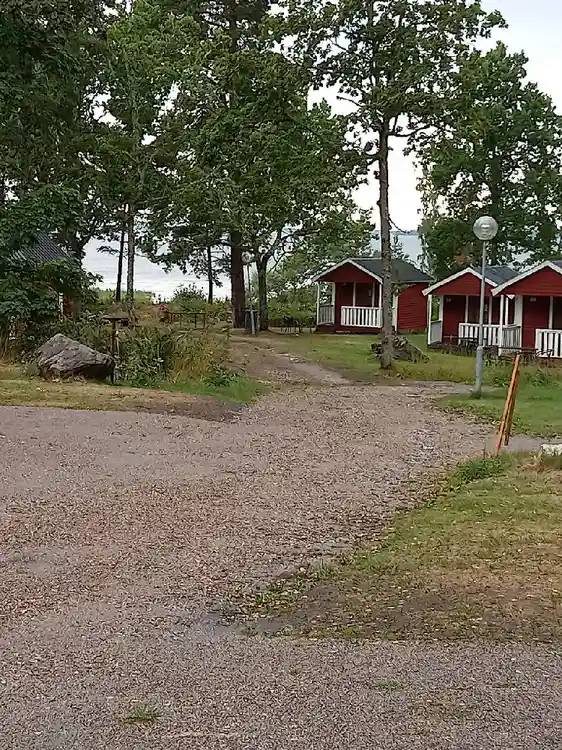 En somrig campingplats med grönt gräs och buskar omger ett rött hus i lantlig miljö.