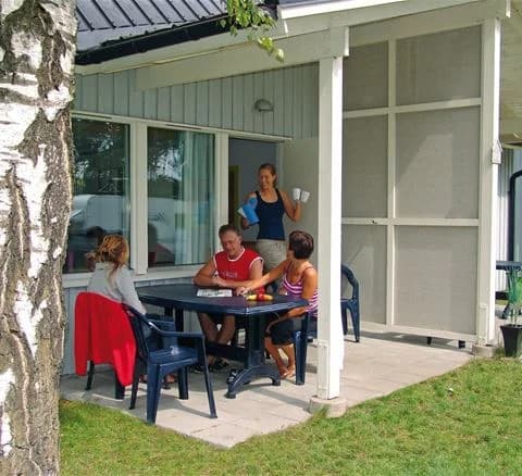 En solig dag vid Ystad camping med stolar och bord placerade på en välskött gräsmatta framför en ljus byggnad. Anpassat för utomhusavkoppling i trädgårds- och lekfull miljö.