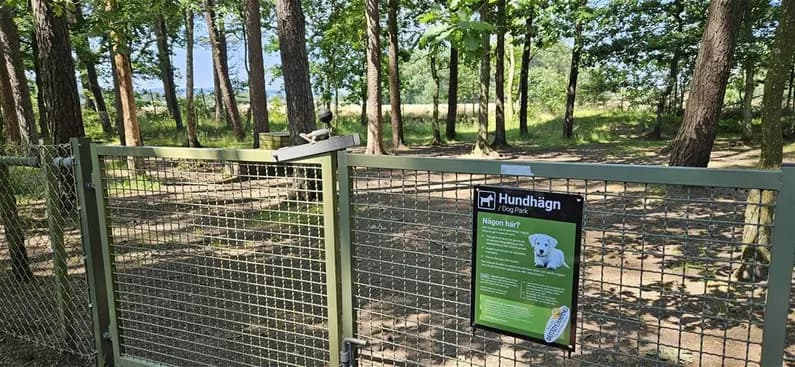 En campingplats i Båstad omgiven av ett metallstängsel, med en grind som leder till en stig.