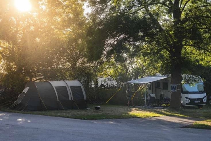 En campingplats vid Kneippbyn Resort Visby med tält och husvagnar bland träden. Skuggiga områden och parkeringsmöjligheter finns tillgängliga.