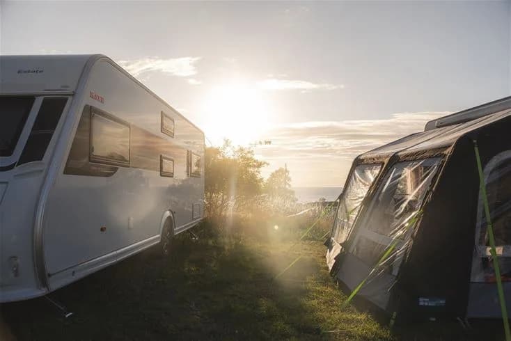 En husvagn parkerad vid Kneippbyn Resort Visby i skymningen, mot en bakgrund av en soluppgång som skapar en stämningsfull atmosfär för en road trip.