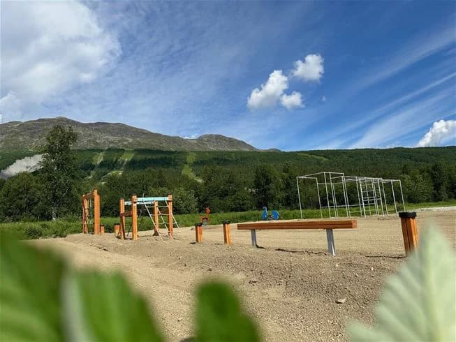 Vy över Camp Kittelfjäll med molntäckt himmel, bergskedjor och skidbackar i bakgrunden. En ensam stolpe syns i förgrunden.