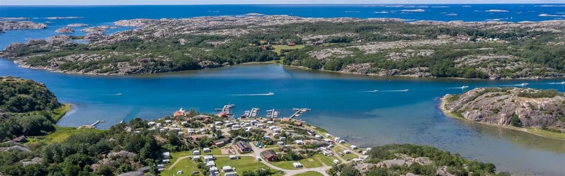 Flygbild över Rörviks camping, som visar en vidsträckt sjö omgiven av frodig grönska. Flera båtar ses flyta i vattnet nära kusten, vilket framhäver områdets natursköna sjöliv.