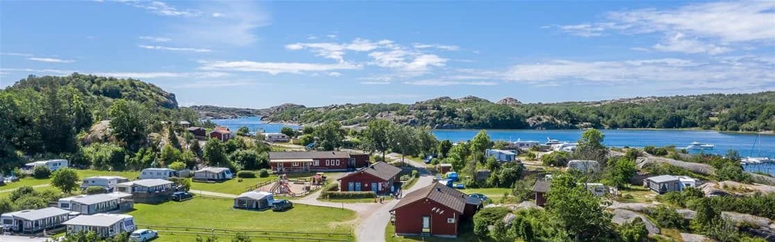 Flygbild över Rörviks camping, omgiven av kustlandskap och sjödistrikt. En bukt syns i bildens mitt och omgivande natur består av grönskande halvöar och vatten. Campingen ligger nära en semesterort och erbjuder panoramavyer över området.