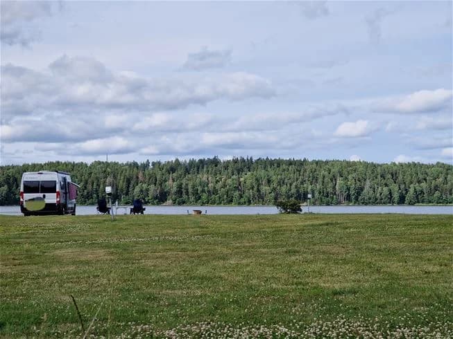 En öppen äng vid Farstanäs Camping & Havsbad med en husbil och en SUV parkerade på gräset under en klar himmel. En idyllisk och lugn naturmiljö för camping och fritidsaktiviteter.