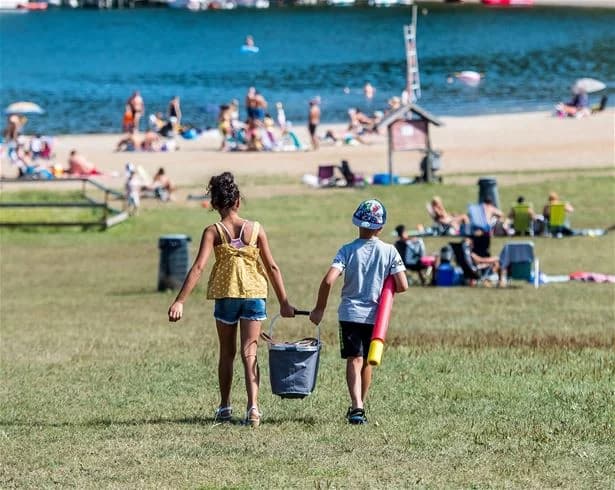 En solig sommardag vid Farstanäs camping & havsbad, där människor njuter av semester och avkoppling på stranden. Vissa solbadar, medan andra deltar i olika fritidsaktiviteter i den natursköna omgivningen.