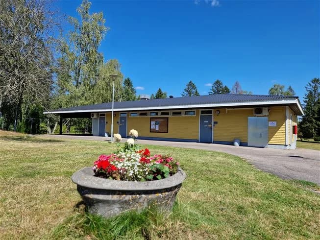 En grönskande campingplats vid havet med ett flertal villavagnar och gräsytor omgivna av träd. En slingrande väg leder genom området, vilket skapar en inbjudande och naturskön miljö för besökare.