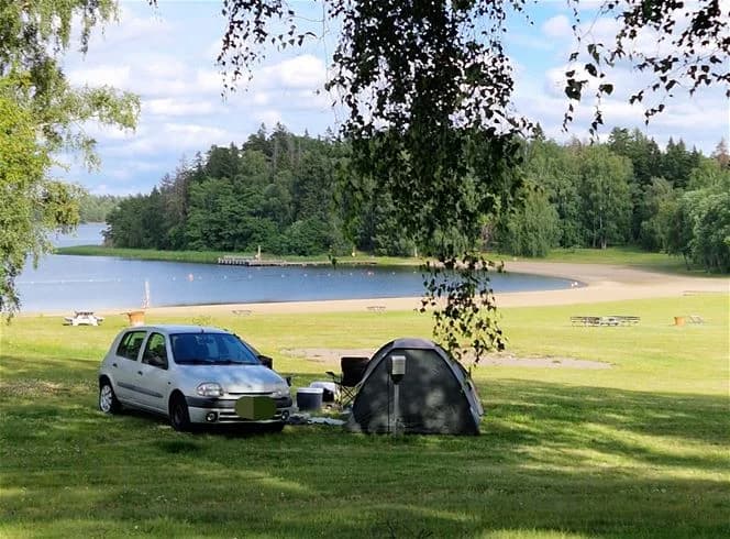 En grön campingplats vid Farstanäs Camping & Havsbad, omgiven av ett frodigt gräsfält och natursköna sjölandskap.