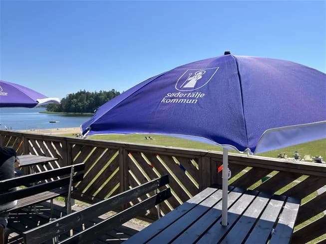 En solig dag vid Farstanäs Camping & Havsbad, med parasoller som ger skugga över uteplatsens bord och stolar, inbjudande för avkoppling i det fria.