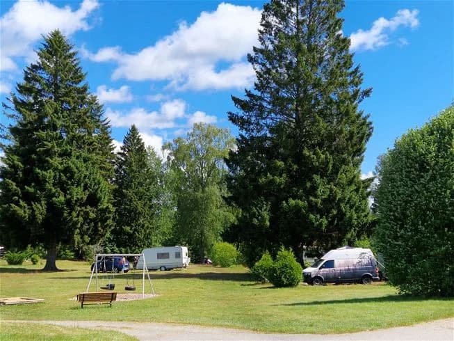 En grönskande campingplats vid stranden med träd, gräs och ängar som omger området, på Farstanäs camping & havsbad.
