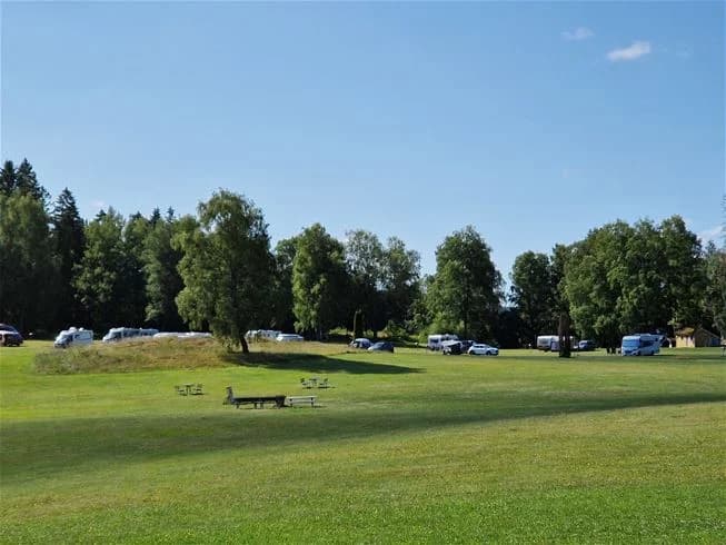 En grönskande campingplats omgiven av träd och öppna ängsmarker på Farstanäs Camping & Havsbad.